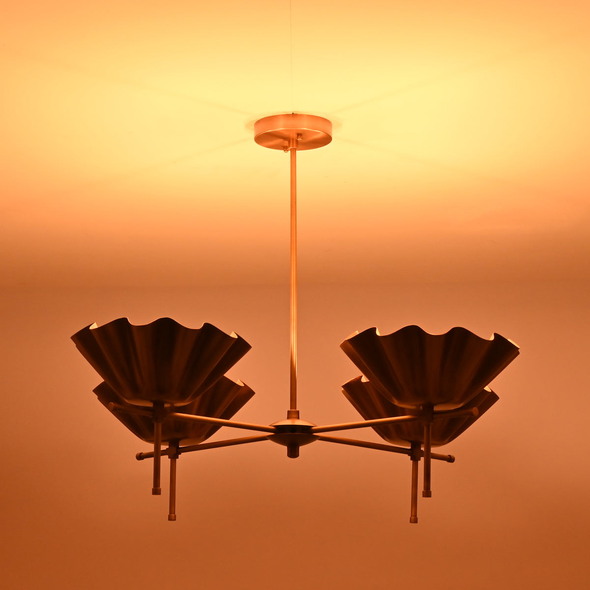 Side view of brass shell shade chandelier illuminated in low light for atmospheric effect