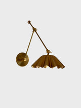 Angled view of adjustable brass swing arm wall sconce with scalloped shade and round wall plate.