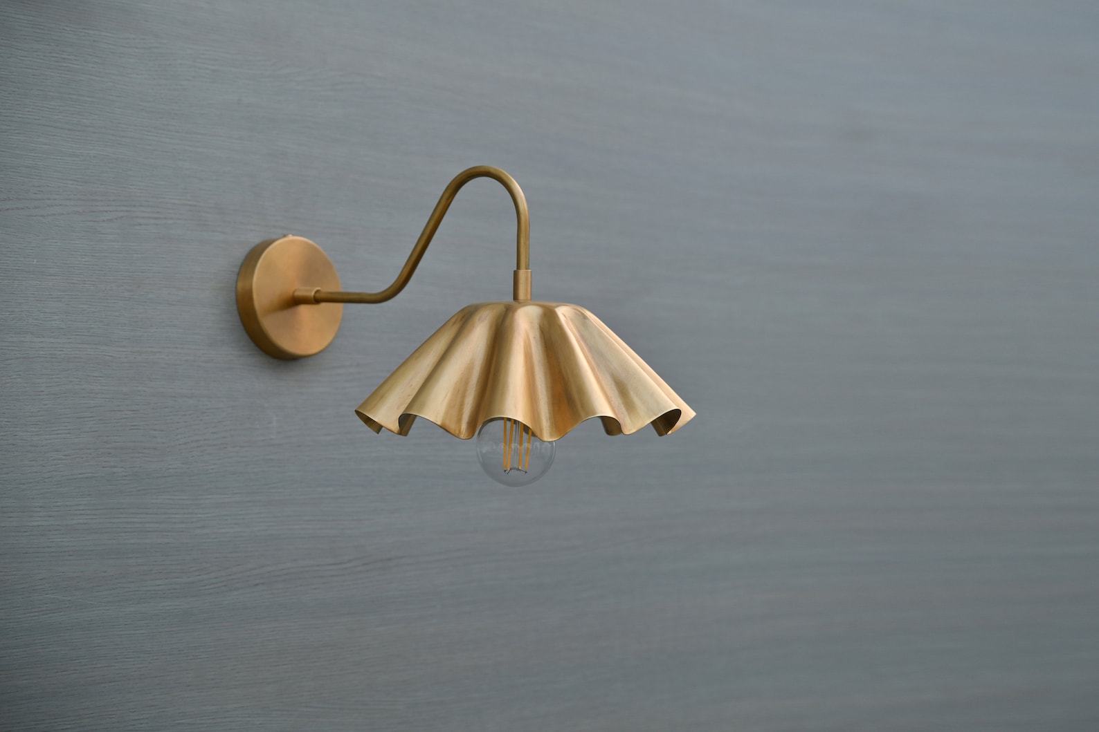 Angled view of handmade brass wall sconce with curved arm and fluted lampshade