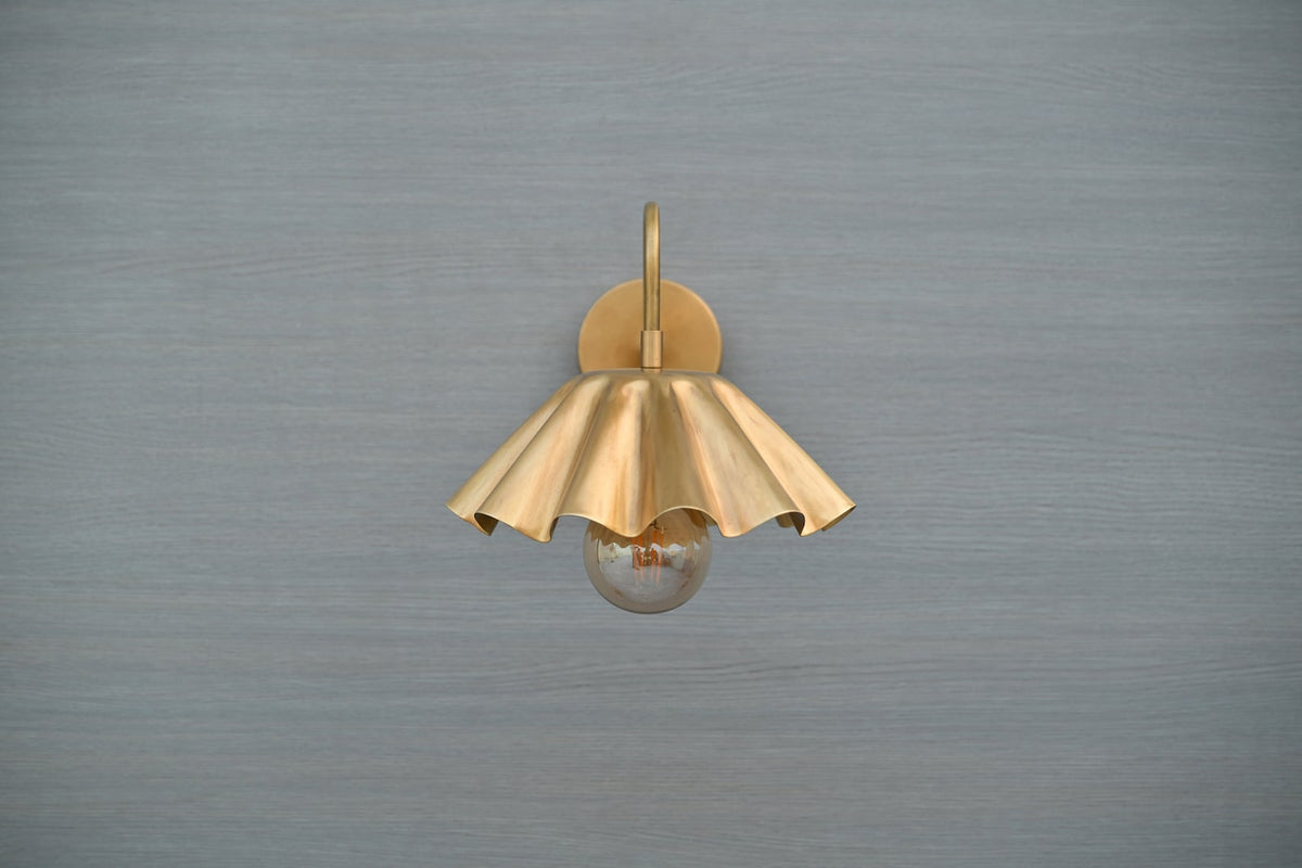 Front view of scalloped brass wall sconce with fluted shade and exposed bulb