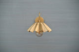 Front view of scalloped brass wall sconce with fluted shade and exposed bulb