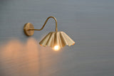 Brass wall sconce with scalloped shade lit with warm bulb, casting ambient light on wall