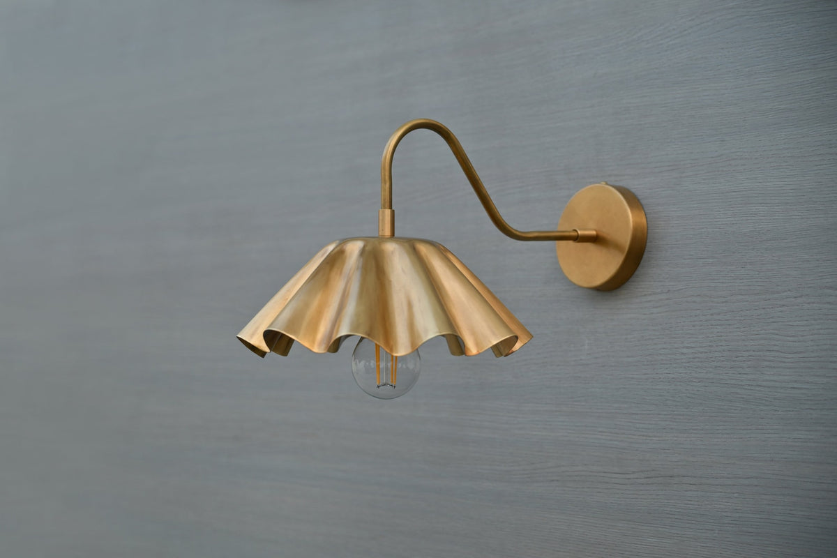 Side angle of brass wall lamp with decorative scalloped shade and exposed bulb