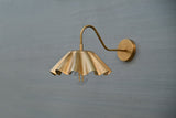 Side angle of brass wall lamp with decorative scalloped shade and exposed bulb