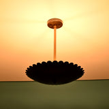 Silhouette view of scalloped brass disc pendant light with dramatic indirect glow