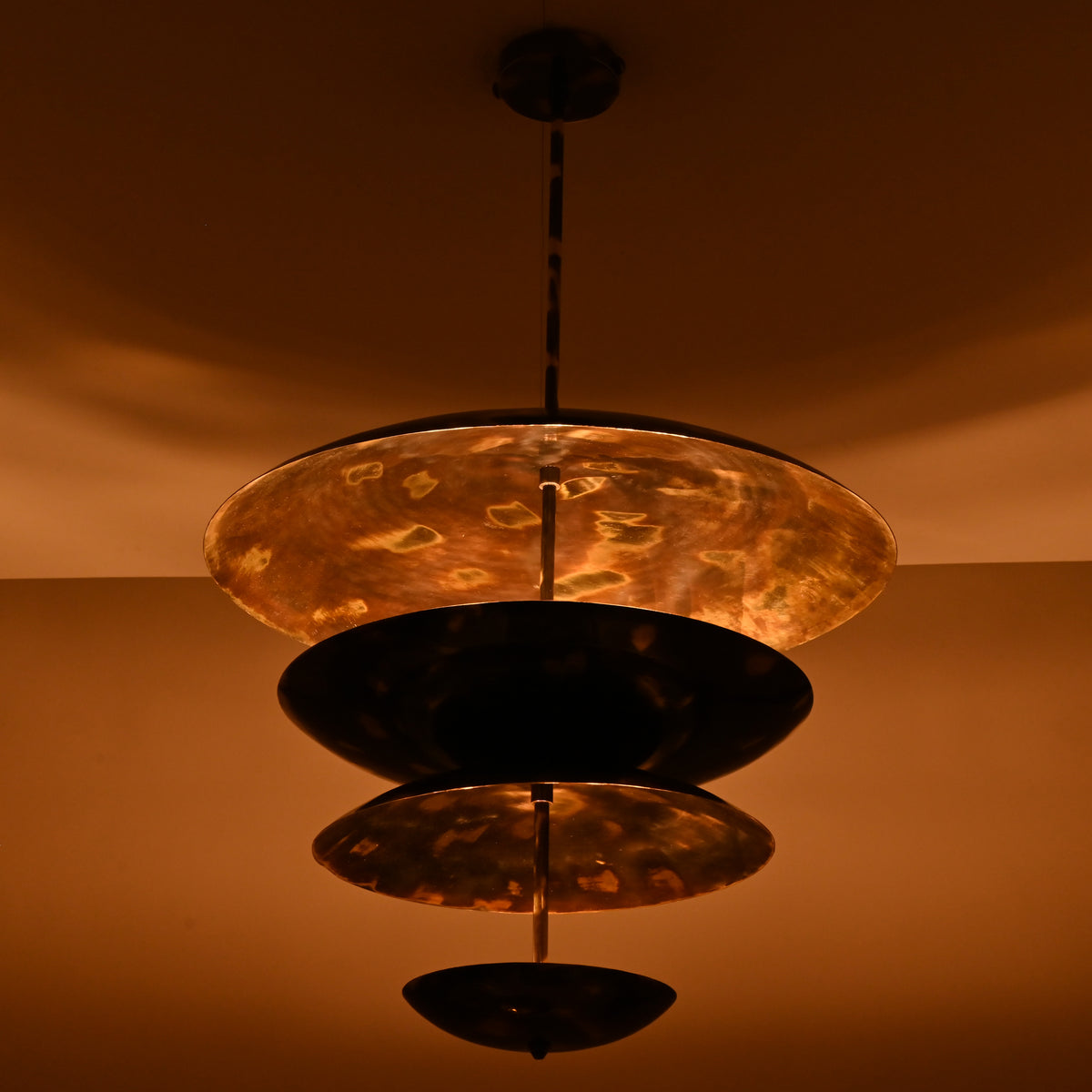 Sculptural layered brass chandelier illuminated at night with warm ambient reflections