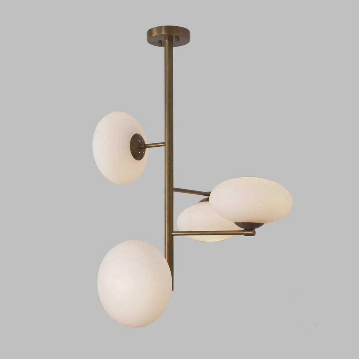 Side angle of a sculptural brass chandelier with milky glass globe shades, highlighting vertical form and softly diffused lighting.