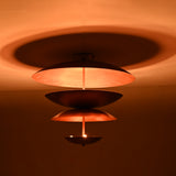 Warm ambient view of the sculptural tiered brass chandelier casting soft indirect light and creating circular shadow halos on the ceiling.