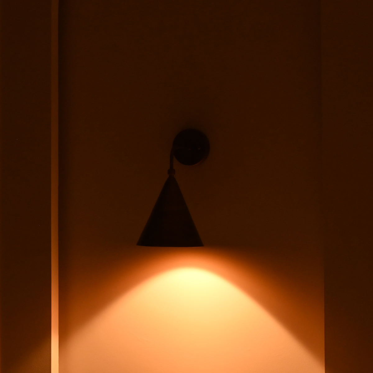 Close view of Seville wall sconce showing lacquer coated brass patina, curved arm and tapered cone shade