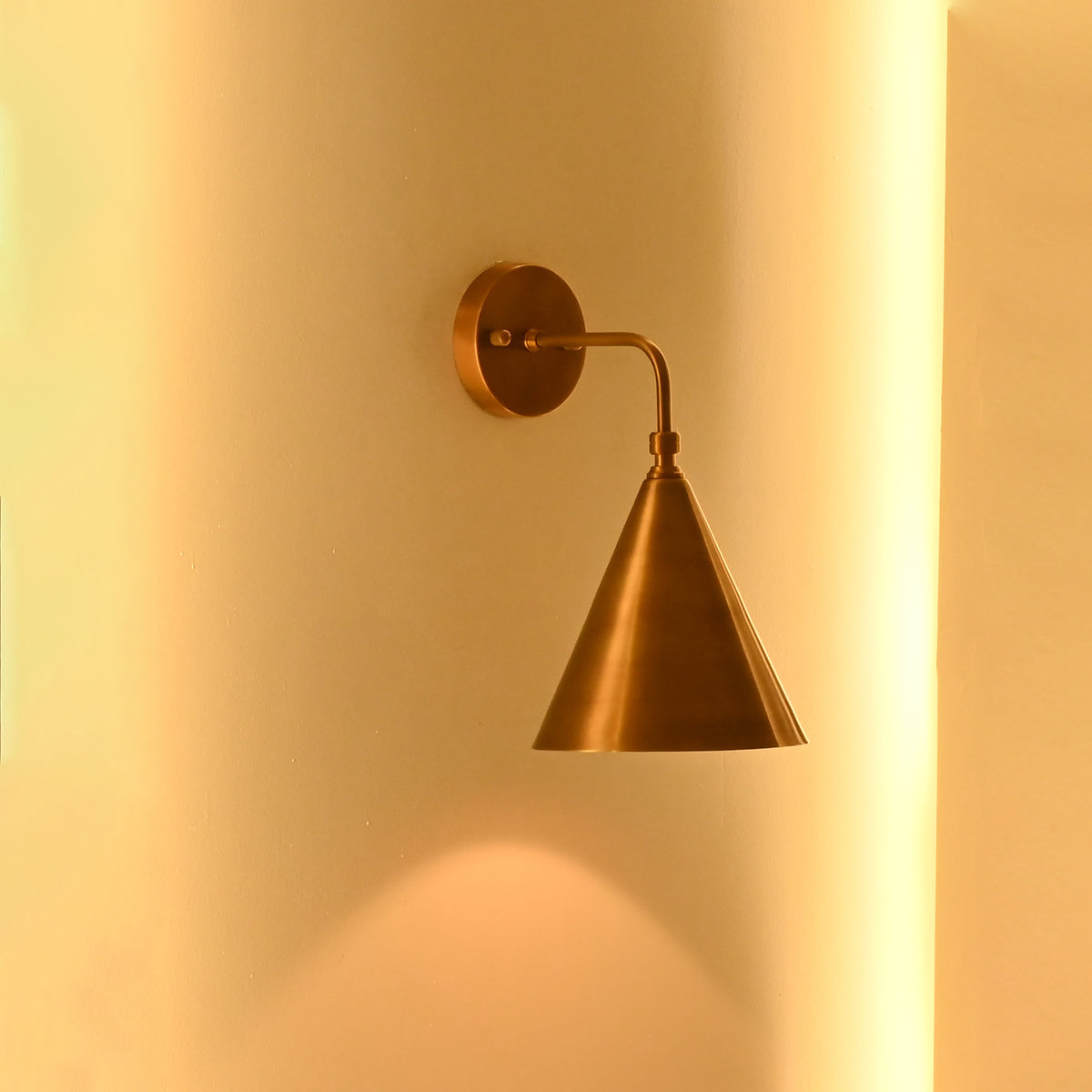 Brass cone wall light displayed in a clean arched wall niche with warm architectural lighting