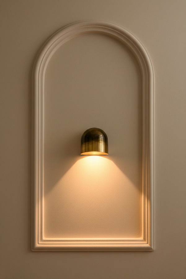 Small brass hallway wall sconce casting a focused cone of warm light from a rounded dome shade