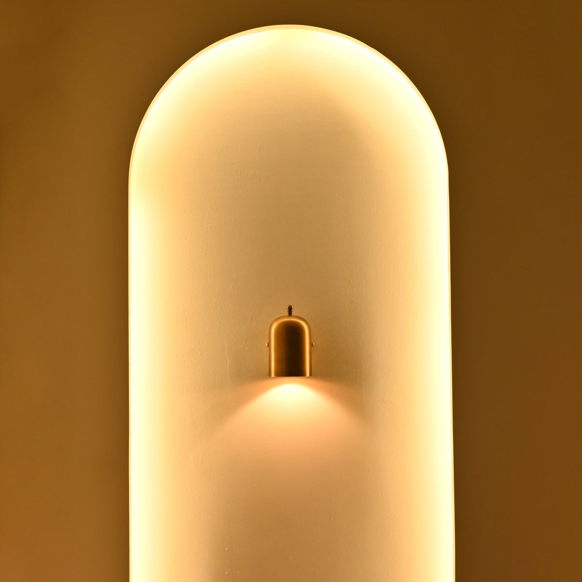 Solid brass cylindrical bedside wall sconce with decorative top finial and warm downward accent lighting
