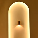 Solid brass cylindrical bedside wall sconce with decorative top finial and warm downward accent lighting