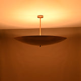 Solid brass disc pendant light illuminated at night with a warm golden glow and indirect lighting.