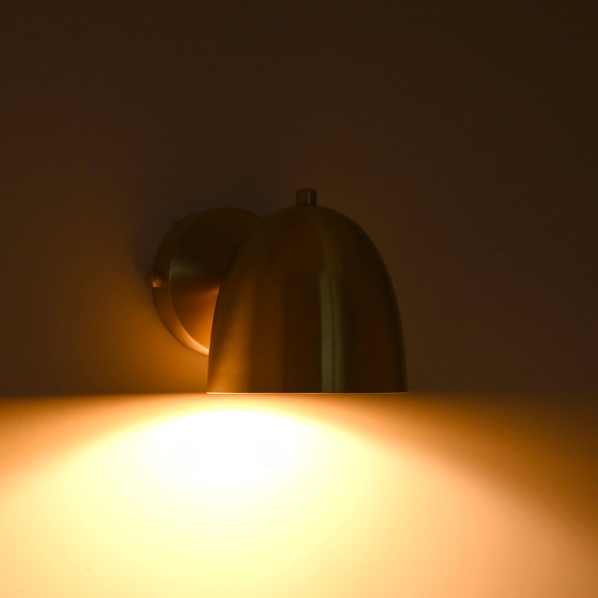 A warm brass wall sconce lamp glowing brightly against a dark brown wall, casting a soft golden light downward.