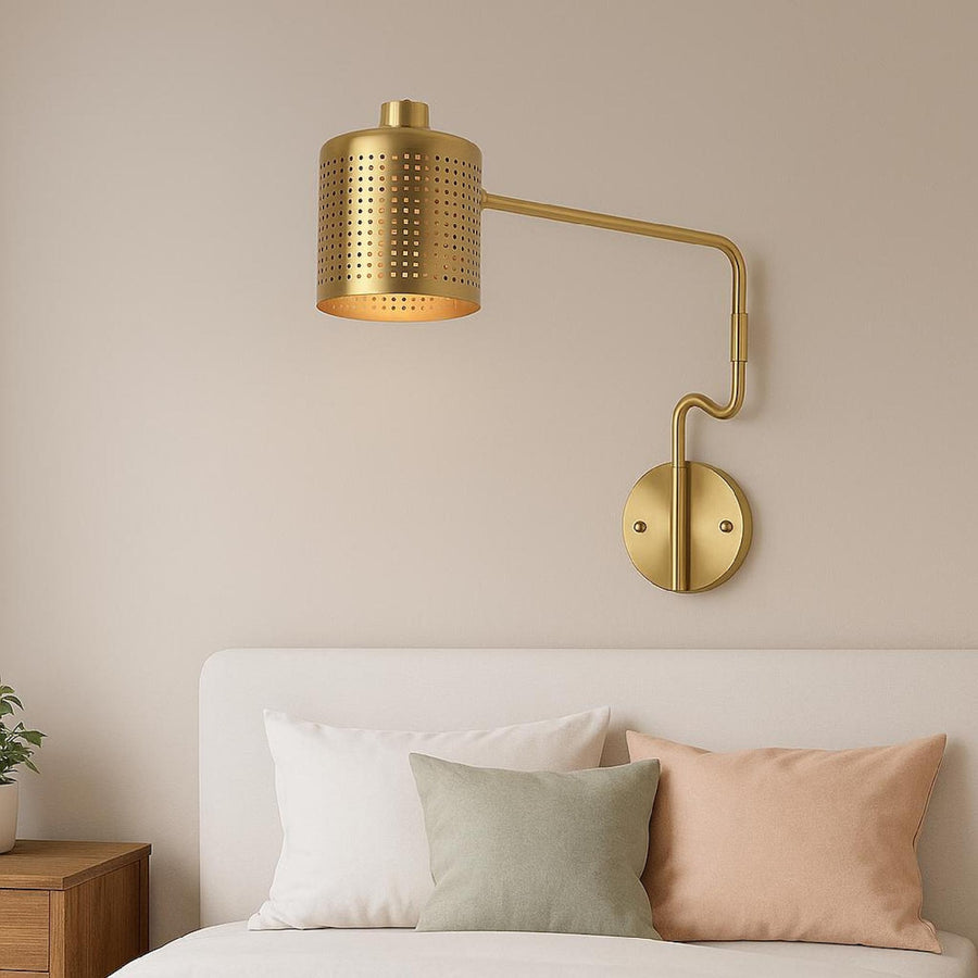 Modern solid brass wall sconce with perforated cylinder shade installed above a bed in a minimalist bedroom