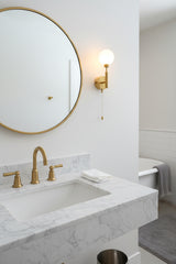 Solid brass wall light with pull chain on off function and soft warm glow from round glass globe shade