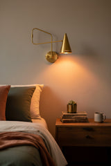 Solid brass swing arm sconce shown illuminated with warm downward glow and tapered cone shade