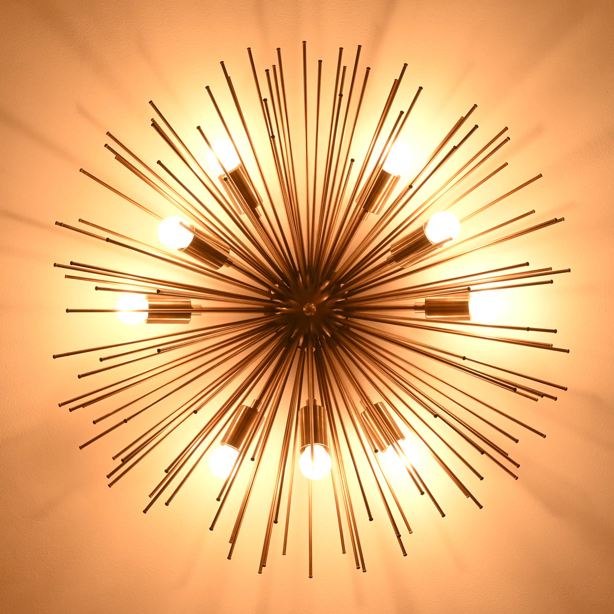 Overhead ceiling view of a glowing sunburst brass chandelier with multiple bulbs