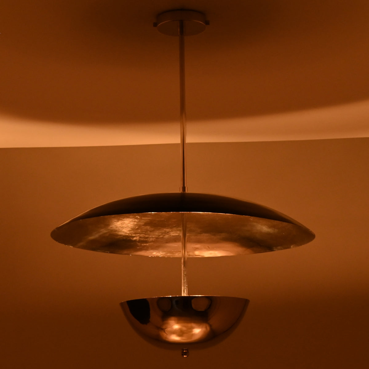 Suspended chrome disc and bowl chandelier glowing warmly in a dimly lit room