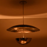 Suspended chrome disc and bowl chandelier glowing warmly in a dimly lit room