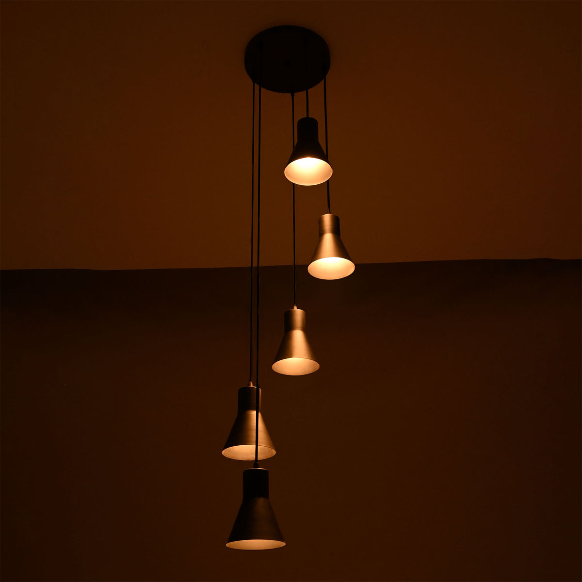Front view of the Sutton Cascade Cone 5 Light Multi Pendant Chandelier illuminated with warm ambient lighting in matte black finish.