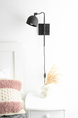 Matte black adjustable wall sconce with dome shade above bedside table, modern industrial wall lamp with plug-in cord