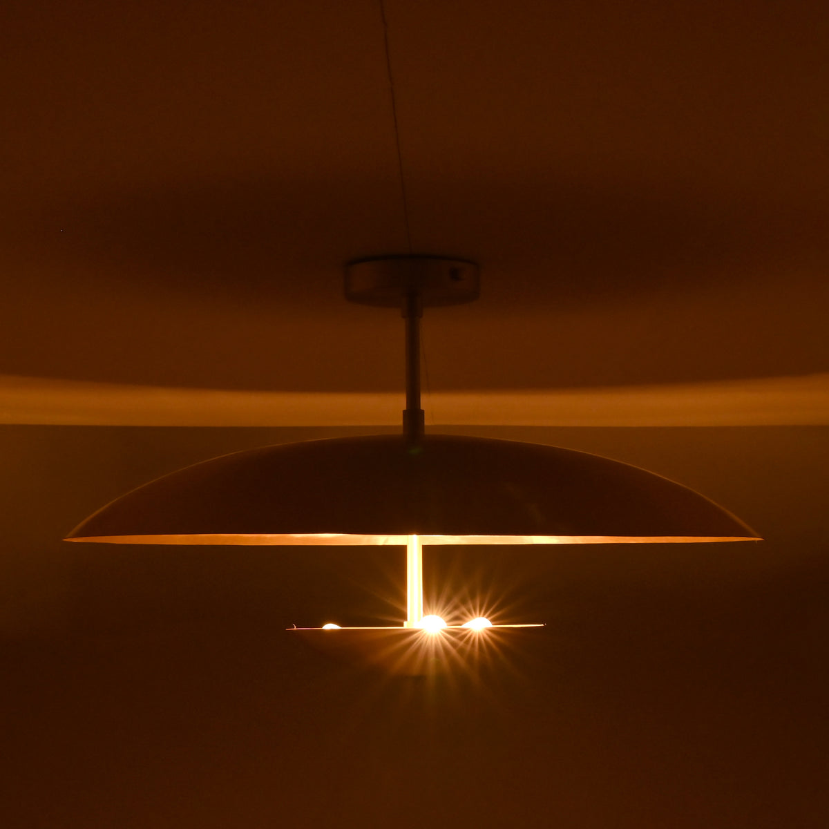 Three-light brass disc flushmount ceiling fixture glowing warmly in a dark interior