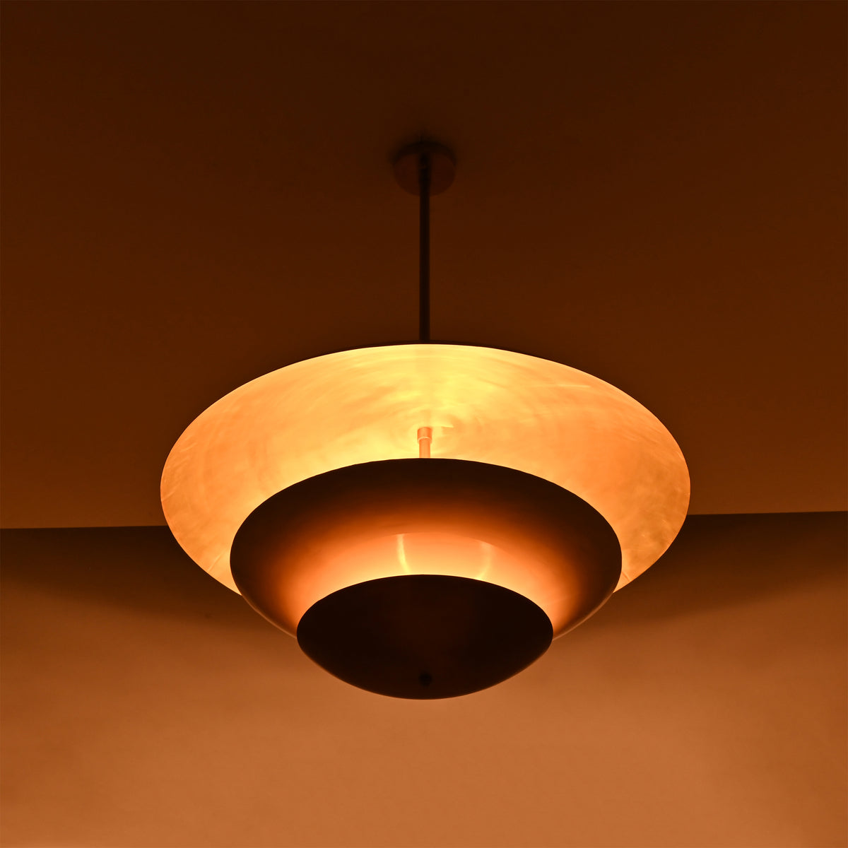Tiered brass pendant light installed above a bedroom, creating soft warm ceiling light with elegant layered style
