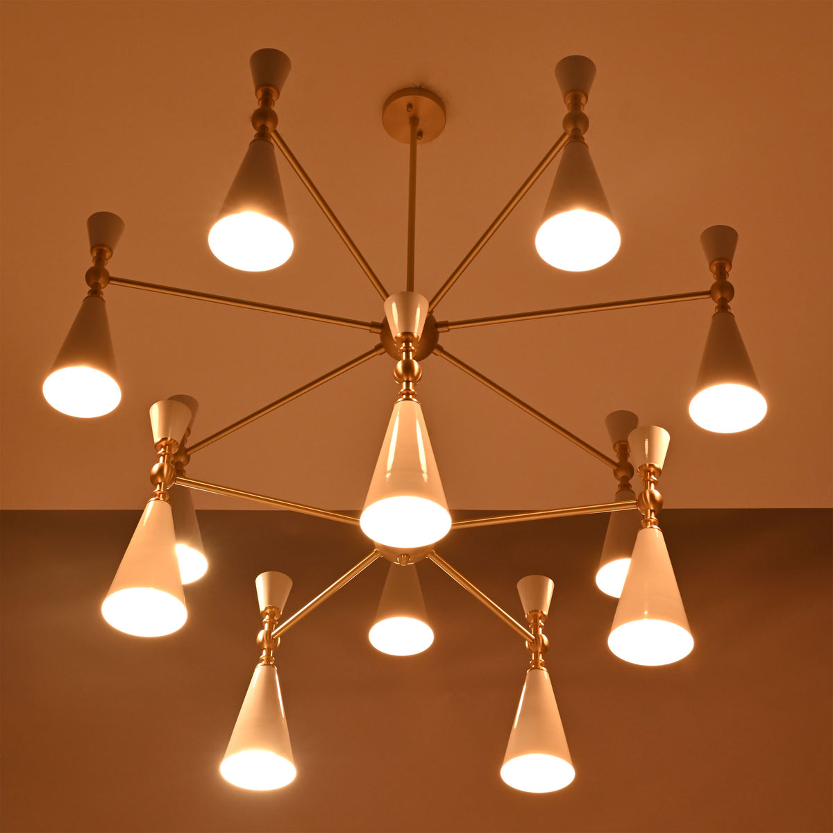 Closeup of two-tier white cone chandelier with warm downward glow and elegant brushed brass connecting arms