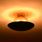 Two-tone brass ceiling light illuminated in low light, revealing polished brass upper dome and blackened disc with warm ambient glow.