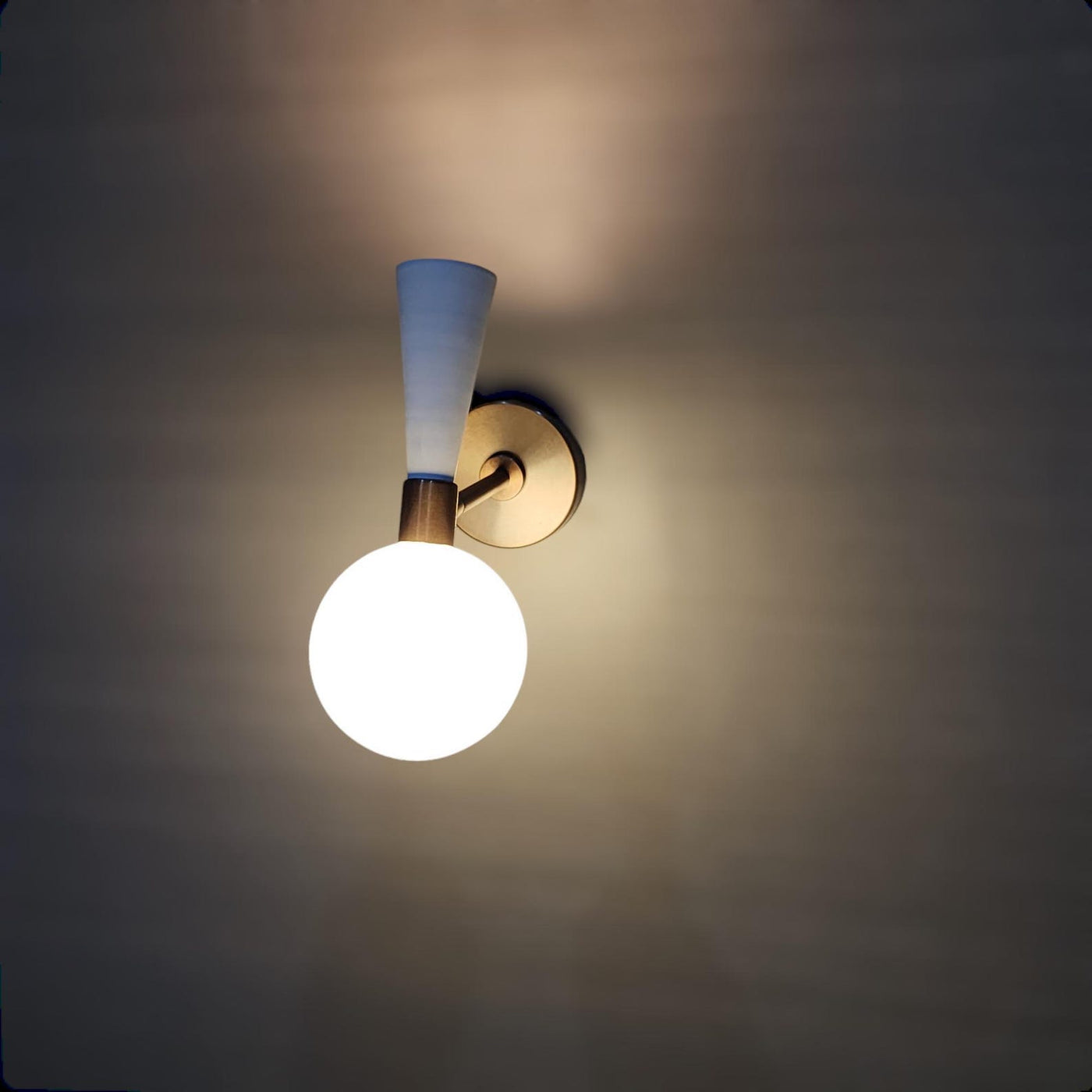 Two-tone brass and white wall sconce with frosted glass globe illuminated, handcrafted by Brass Leaf Studio