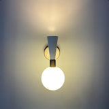 Two-tone brass and white globe wall sconce mounted on wall, glowing softly for warm ambient lighting