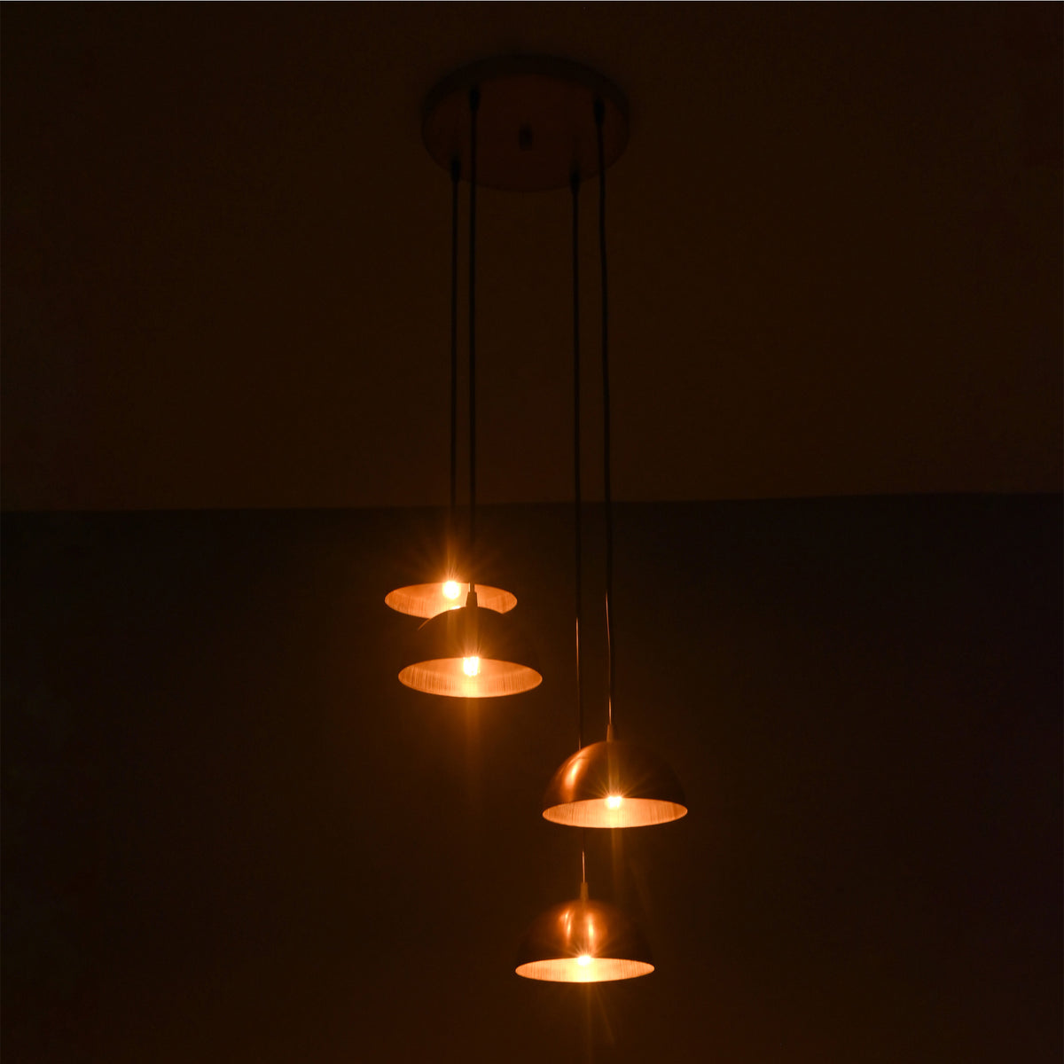Verona Cascade Dome Multi Pendant Chandelier illuminated against a dark background, highlighting warm focused lighting from four brass dome shades.