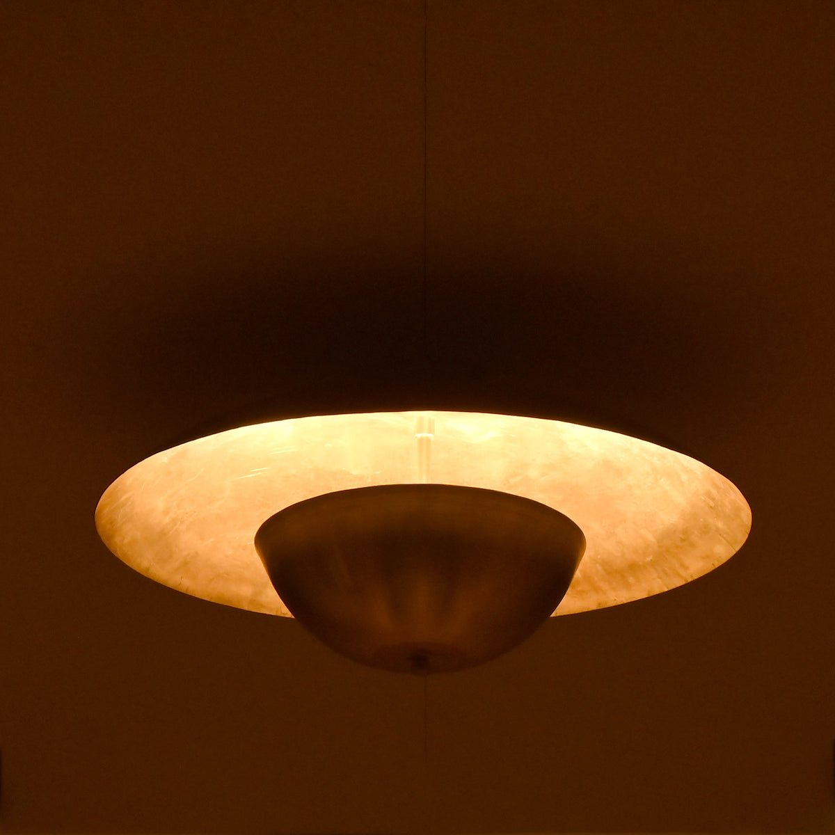 Side view of illuminated raw brass ceiling fixture casting soft warm ambient light across the ceiling