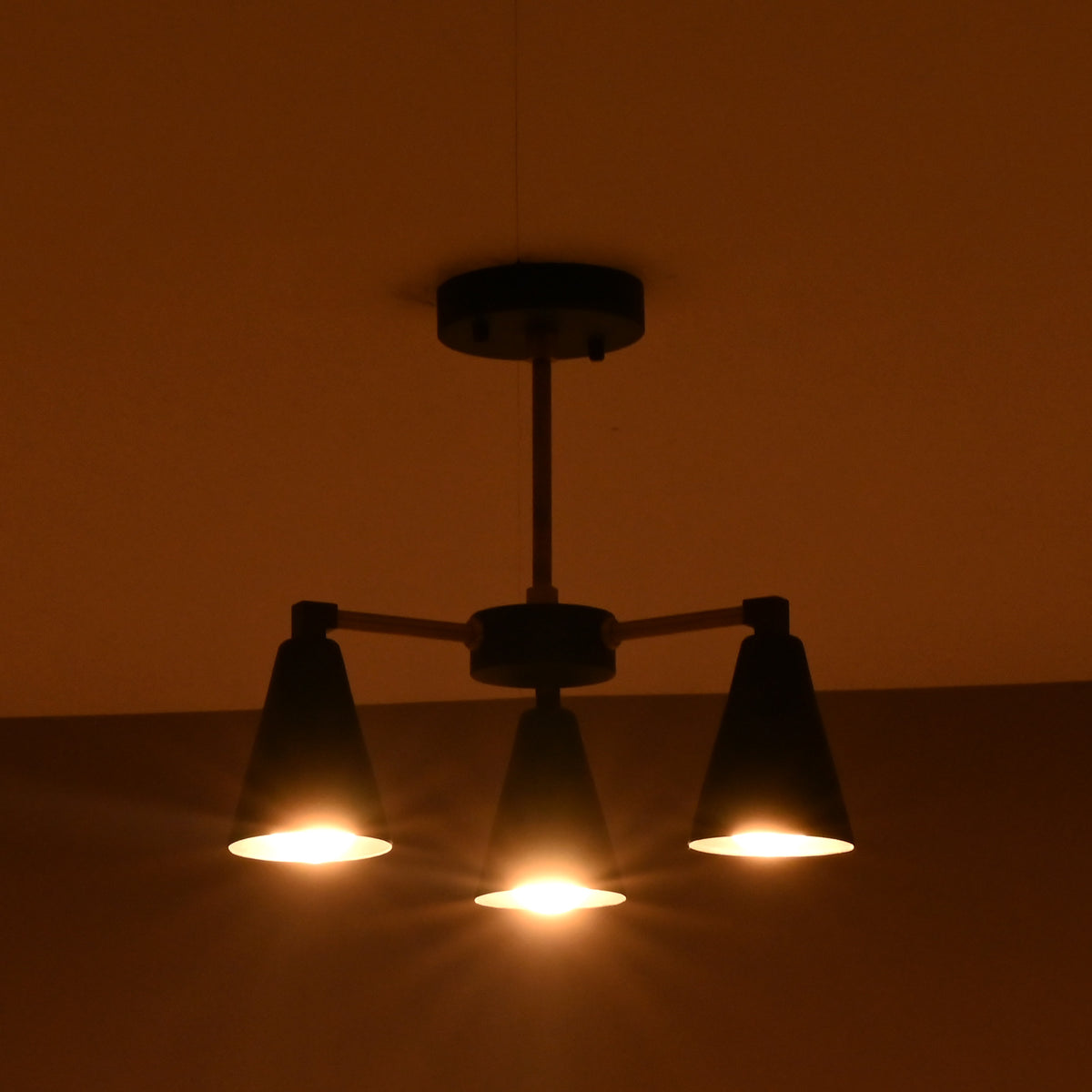 Ambient warm glow from 3 light brass and black ceiling chandelier in dark interior setting