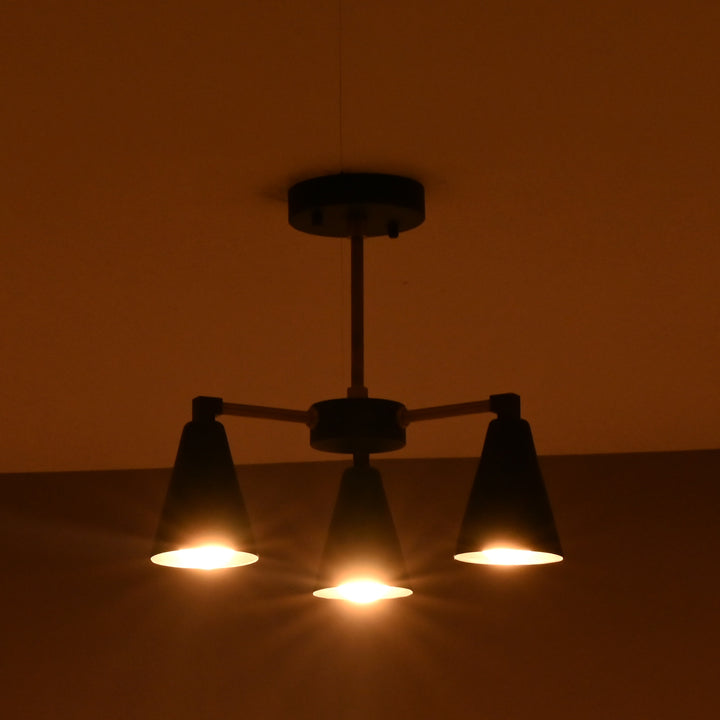 Ambient warm glow from 3 light brass and black ceiling chandelier in dark interior setting