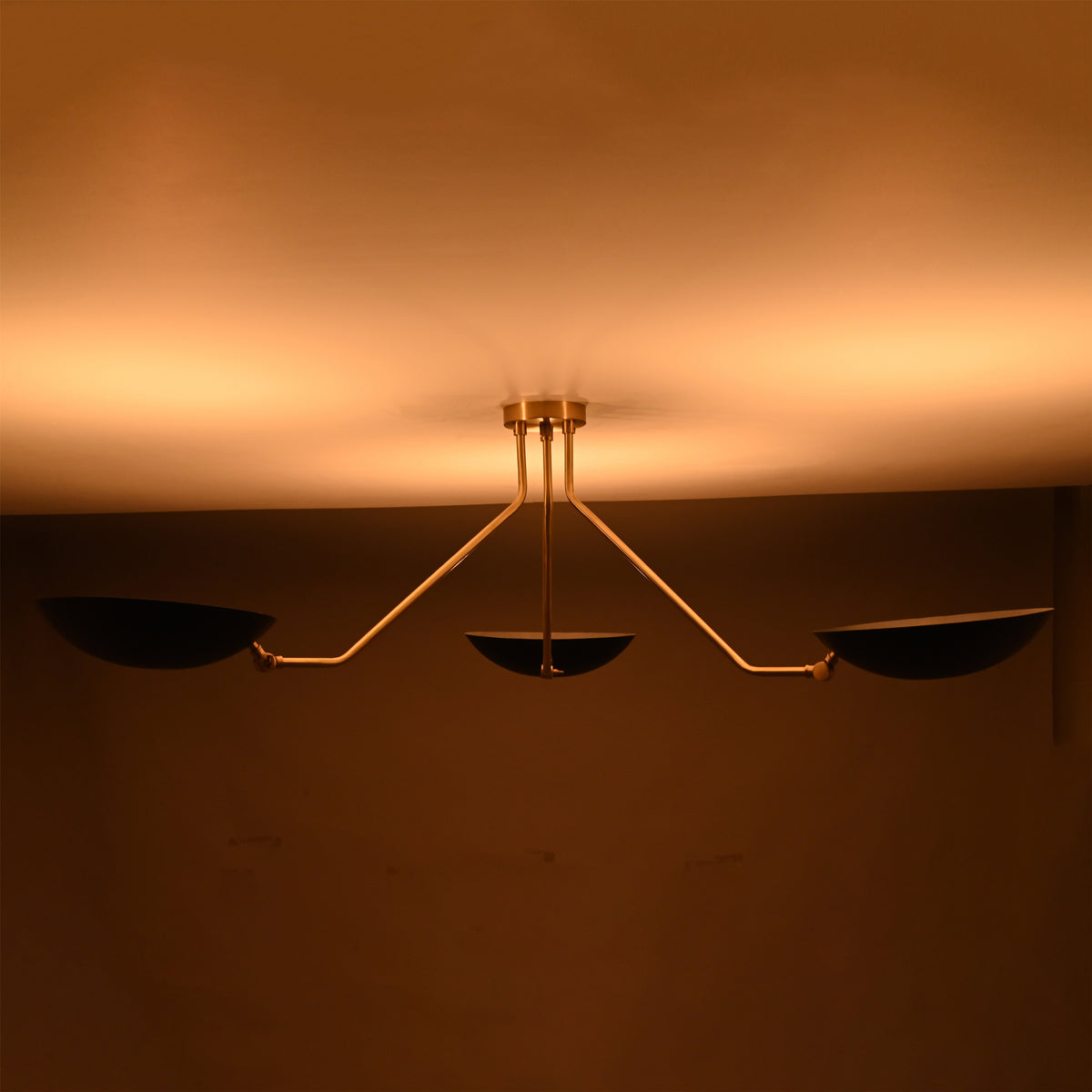 Night view of black and brass chandelier emitting soft golden ambient light across the ceiling.