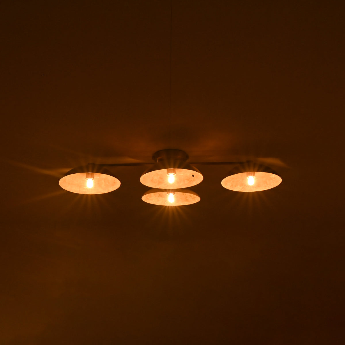 Minimalist ceiling shot showing 4-light brass flush mount chandelier lit warmly in a dimmed setting.