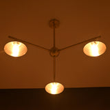 Brushed brass 3-light chandelier illuminated in warm ambient lighting, showcasing cone shades in a dark room.