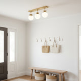 Warm glow linear globe ceiling light with three illuminated white glass globes and brushed brass structure